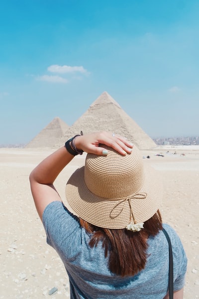 Standing in front of the pyramid during the day a woman in a blue coat
